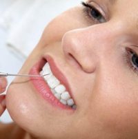 Dentist using dental tool on women's teeth.